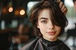 © Alexander Odessa  - cheerful woman with short brunette hair sitting in a hairdresser's cape in a beauty salon, getting her hair cut by a professional hairdresser, beauty salon.