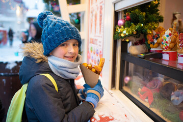 Wall Mural - a boy in winter clothes holds delicious churros in his hands, at a Christmas market in the snowy winter.