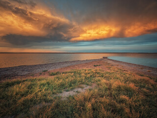 Wall Mural - dramatic burning clouds above lake and wild spit with grass