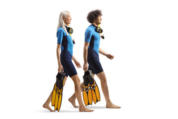 Sticker - Full length profile shot of a man and woman in wetsuits carrying fins and walking