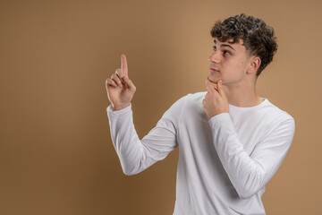 Wall Mural - Portrait of one caucasian man 20 years old looking to the camera in front of almond color studio background smiling wearing casual shirt point on copy space