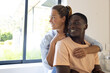 © Wavebreak Media - A diverse couple is smiling and embracing each other near window, copy space