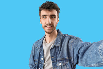 Wall Mural - Handsome young man taking selfie on blue background, closeup