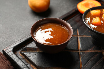 Board with bowl of sweet apricot jam on black background