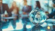 © tashechka - Crystal globe on a reflective office meeting table with blurred silhouettes of businesspeople in the background.