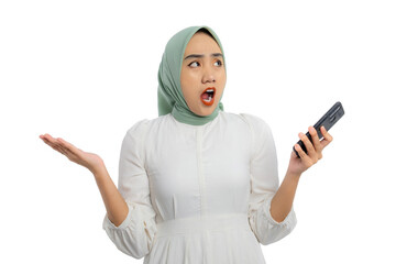 Wall Mural - Surprised young Asian woman in green hijab and white blouse holding smartphone with open mouth and raised hand isolated on white background