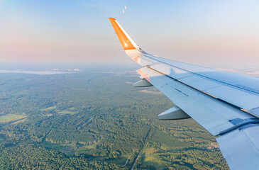 View of airplane wing, blue skies and green land during landing. Airplane window view.