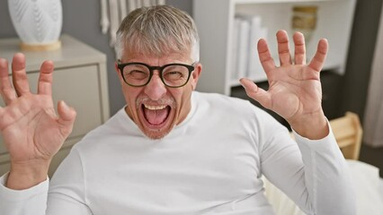 Canvas Print - Middle-aged, grey-haired man, smiling with a funny, sexy expression, does a claw gesture in his pyjama, adding an aggressive twist in the bedroom of his cosy home