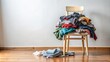 © tnihousestudio - Chair covered with a pile of messy clothes in a simple room.