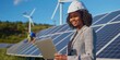 © YURIMA - Engineer working on a project involving solar panels and wind turbines, focusing on renewable energy. This female professional is outdoors using a tablet, optimizing green technology
