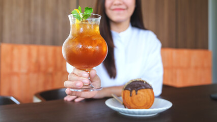 Wall Mural - Closeup image of a woman holding a glass of iced lemon tea with chocolate Timber Ring Croissant on the table