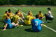 © master1305 - Active Youth Engagement. Children sitting on grass and listening to female football coach instructions, learning soccer game strategies and skills. Sport, school, childhood, active lifestyle concept