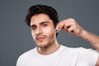 © Prostock-studio - Skin nutrition. Young man applying organic essential serum on face with pipette, free space