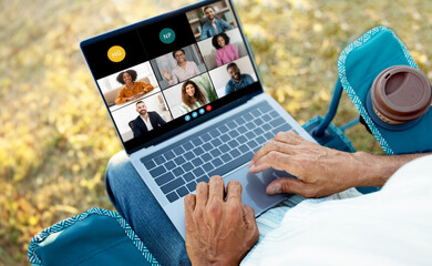 Wall Mural - Senior man is sitting outside, participating in a virtual business meeting on his laptop. Several colleagues are visible on the screen, engaging in conversation.