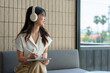 © Phimwilai - Happy Asian woman planning event on tablet While sitting on the sofa at the coffee shop Relaxed smiling young woman with headphones Relaxed learning in the morning, holiday work concept.