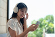 © Phimwilai - Happy Asian woman listening to music on mobile phone while sitting on sofa at coffee shop Relaxed smiling young woman with headphones in the morning Holiday relaxation concept.