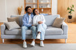 © Prostock-studio - Indian man and woman are seated on a beige couch in a living room. They appear to be engaged in conversation or watching TV, looking at copy space