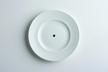 A minimalist white plate with a single black dot in the center, set against a smooth white background.