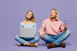 © ViDi Studio - Full body young couple two friends family IT man woman wear pink blue casual clothes together sitting use mobile cell phone work on laptop pc computer look aside isolated on plain purple background.
