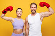 © ViDi Studio - Young cool strong fitness trainer instructor sporty two man woman wear blue clothes boxing gloves show hand biceps spend time in home gym isolated on plain yellow background Workout sport fit concept