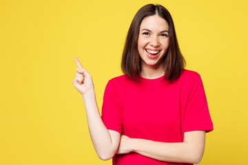 Young happy smiling cheerful woman she wear pink t-shirt casual clothes point index finger aside on workspace area mockup isolated on plain yellow orange background studio portrait. Lifestyle concept.