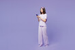 © ViDi Studio - Full body young calm woman wear pyjamas jam sleep eye mask rest relax at home hold in hand use mobile cell phone isolated on plain pastel light purple background studio. Good mood night nap concept.