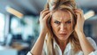 © tashechka - A stressed woman with her hands on her head, looking frustrated in a modern office setting, expressing workplace tension.