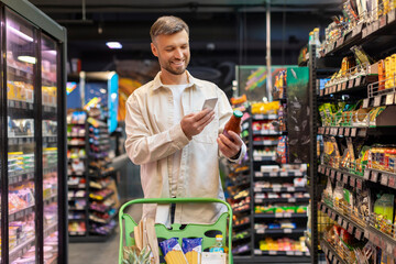 middle aged man shopping for products and scanning barcode with smartphone at supermarket., checking