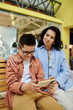 © Bliss - A mother and her son with Down syndrome are sitting together on a bench in a shopping mall, looking at a phone.