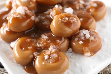 Wall Mural - Tasty candies, caramel sauce and salt on wooden table, closeup