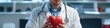 © Dalibor - A close-up of a cardiologist in a white coat holding a detailed anatomical heart model. The background features a blurred medical-themed setting with a stethoscope visible around the doctor's neck.