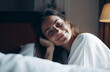 © larrui - A woman is laying on a bed with her head on her hand. She is smiling and looking at the camera