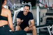© bnenin - Photo of a smiling male talking to his female partner, sitting on a bench, resting from a workout at the gym.