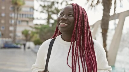 Canvas Print - A smiling black woman with red braids outdoors in a city wearing a white sweater.