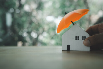 Poster - An insurance agent is holding a orange umbrella over a wood house model. Property insurance concept. Protection of housing or house. Security and safety housing insurance Service