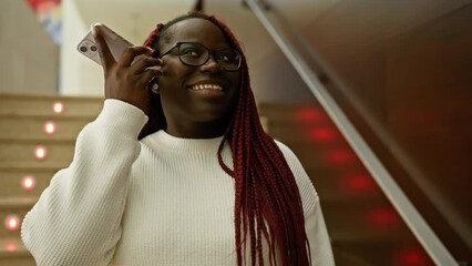 Sticker - Smiling african woman with braids talking on a smartphone in a modern indoor office setting.