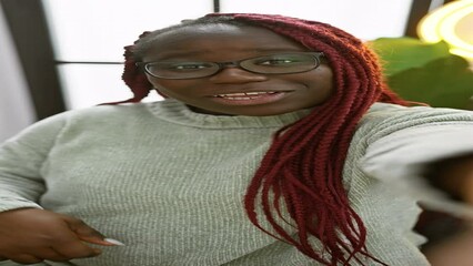 Poster - African american woman with braids wearing glasses and a sweater posing indoors with a happy expression