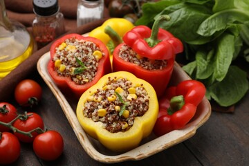 Wall Mural - Quinoa stuffed bell peppers in baking dish, basil and tomatoes on wooden table, closeup