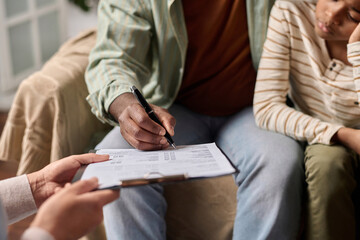 Side view closeup of unrecognizable Black man signing document on clipboard in clinic copy space