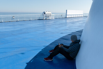 Wall Mural - Traveler with smartphone on deck of a cruise ship during sailing to Faroe islands. Calm ocean and clear blue sky