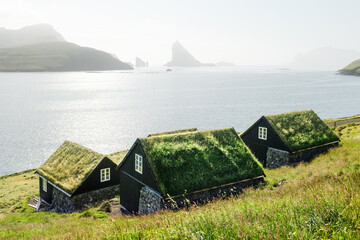 Wall Mural - Traditional faroese grass-covered cottages in the village Bour. Drangarnir and Tindholmur sea stacks on background. Vagar island, Faroe Islands, Denmark. Landscape photography