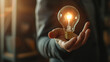 © Kiangdeb - Businessman holds a glowing lightbulb, symbolizing innovation and creativity in a modern setting.