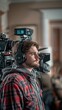 © neatlynatly - A focused man wearing headphones and a plaid shirt operates a professional camera setup in a cozy indoor setting.
