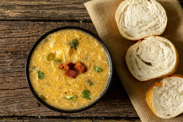 Caldo de Kenga Cassava broth with shredded chicken, typical Brazilian food known as (Caldo de Quenga), in a black pot on top of a rustica with a spoon and slices of bread,  with selective focus