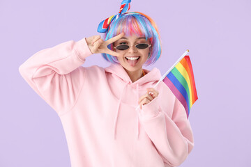 Wall Mural - Beautiful young woman with LGBT flag showing victory gesture on lilac background