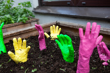 Colorful hands reach up from the soil in a garden, creating a whimsical and slightly eerie scene. 