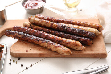 Wall Mural - Board of tasty grilled sausages on white wooden background
