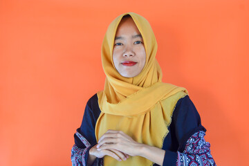 A friendly and successful Asian Muslim woman wearing a batik shirt with an orange background exclaimed excitedly while raising her two index fingers upwards, showing something.