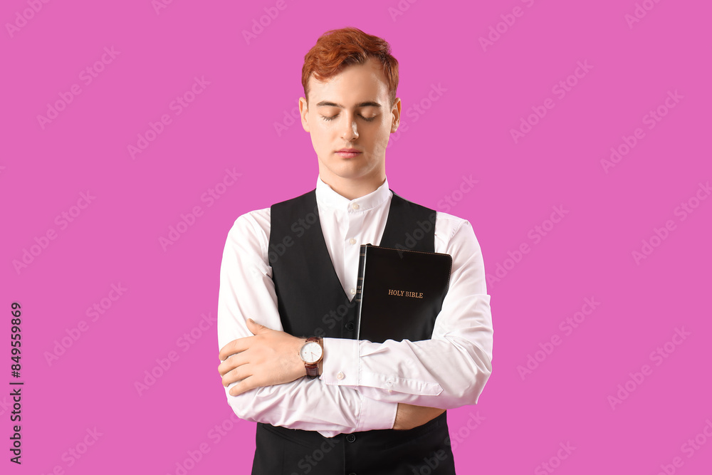Young redhead man with Bible on purple background