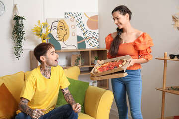 Happy young couple with tasty pizza sitting on sofa at home